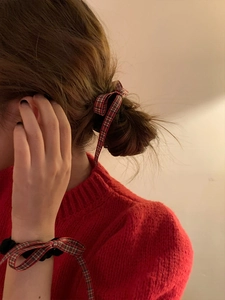 Red and green plaid bow scrunchie shown styled on a bun and worn on the wrist