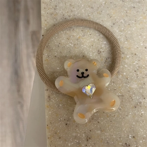 Detail of a brown elastic hair tie with a cute cream bear charm and a sparkling heart rhinestone
