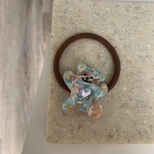 Detailed macro view of an elastic hair tie with a marbled bear pendant and heart rhinestone