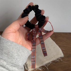 Close-up of black velvet scrunchie featuring a classic red and green plaid ribbon bow