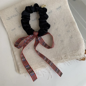 Close-up of velvet hair scrunchie with red plaid ribbon and gold metal charm
