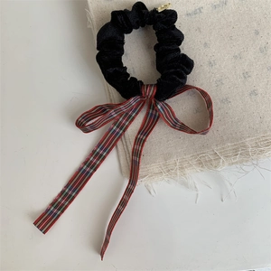 Detail of black velvet scrunchie with classic red and green plaid bow and gold metal buckle