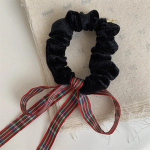 Detailed shot of black velvet scrunchie with red plaid bow and gold metal tag
