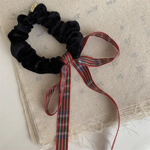 Detail of red plaid bow scrunchie with velvet texture and gold metal charm