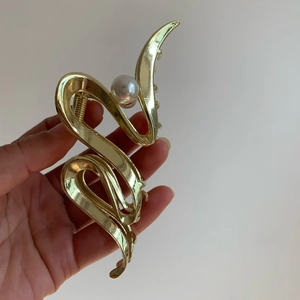 Close-up of a large gold metallic hair claw clip with wave design and white pearl detail