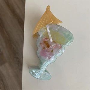 Close-up of a blue acetate hair claw clip shaped like a cocktail with a yellow umbrella