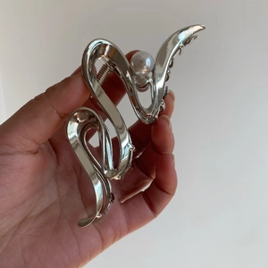 Silver metallic wave shark hair clip with pearl detail held in hand for hair styling