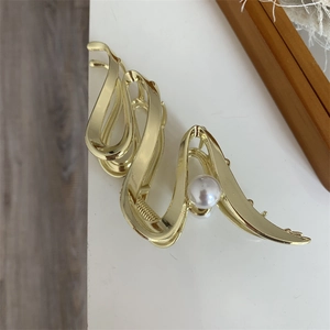 Detailed close-up of golden wavy metal hair claw with pearl accent on a desk