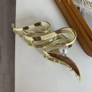 Detail of a wavy gold metal hair claw clip featuring a single polished pearl accent