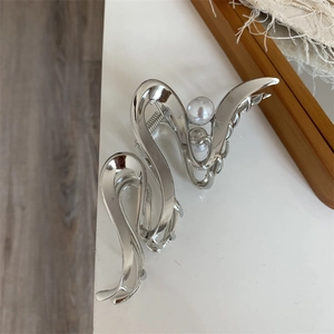 Detailed close-up of a silver wavy metal hair claw clip with an elegant white pearl accent