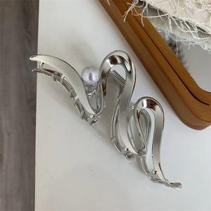 Detail shot of silver wave-shaped hair claw clip with pearl on wooden tray