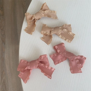 Pink and champagne satin bow hair clips with ruffled edges on light wooden surface