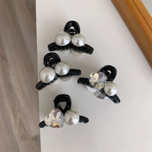 Dettaglio di mini mollette per capelli con perle e cristalli a cuore su base nera lucida