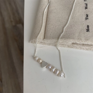Dettaglio macro del ciondolo a cuore argento e perle barocche su catena a maglie