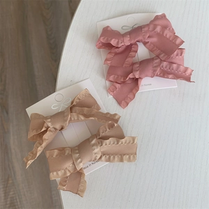 Detail of pink and beige bow hair clips with ruffled edges on a white display card