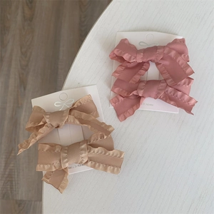 Detail of pink and brown bow hair clips on white card with scalloped ribbon edges