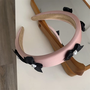 Detail of pink padded headband with black ribbon bows and elegant pearl accents