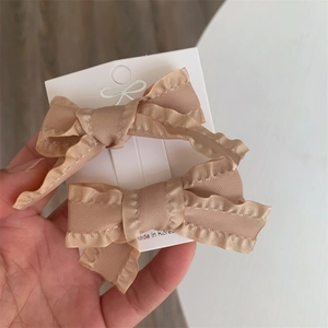 Close-up of two elegant pink bow hair clips with wavy edges on a branded display card