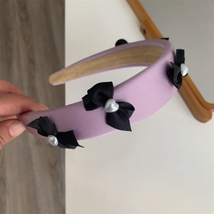 Detail of purple padded headband with black satin bows and heart-shaped pearls