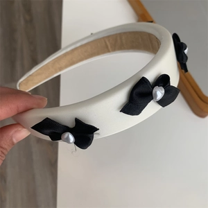 Detail of white satin padded headband featuring black bows and heart pearl accents