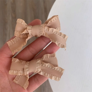 Pair of champagne pink bow hair clips with ruffled edges and satin finish for women