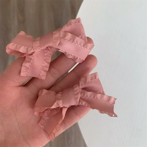 Close-up of pink satin bow hair clips featuring delicate ruffled edges and silky texture
