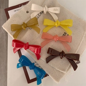 Détail de barrettes nœuds en acétate coloré avec lettrage artisanal sur lin vintage