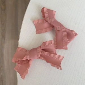 Detail view of pink satin bow hair clips with ruffled edges on a white textured background