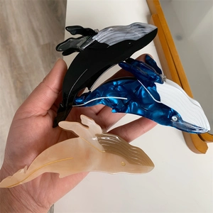 Detailed view of three whale-shaped acetate hair claws with marble textures in a hand