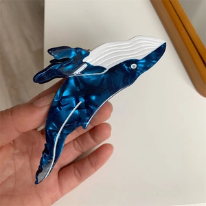 Macro detail of whale-shaped hair claw clip with blue marble texture and cream white finish