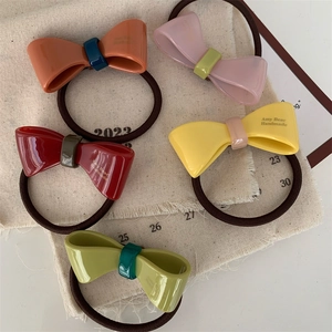 Five colorful handmade acetate bow hair ties in vibrant tones on a linen fabric background