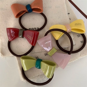 Detail view of five colorful bow hair ties on rustic linen background featuring handmade text