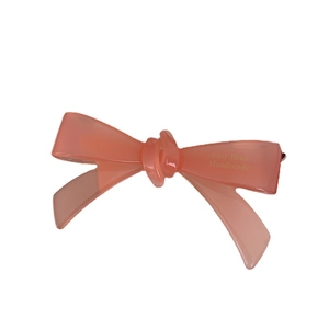 Barrette à cheveux nœud en acétate rose pêche avec logo doré sur fond blanc