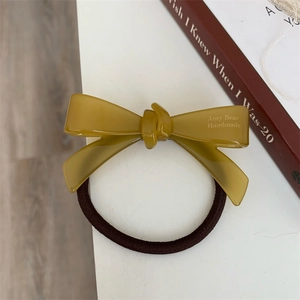 Détail d'un élastique à cheveux fait main avec nœud jaune gingembre et logo gravé
