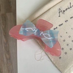 Detail der Haarklammer aus rosa Acetat mit blau karierter Schleife auf weißem Grund