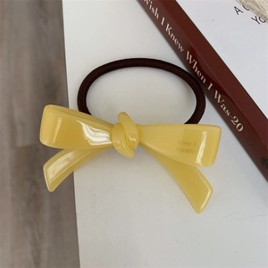Vue rapprochée d'un élastique à cheveux nœud jaune en acétate avec lettrage fait main