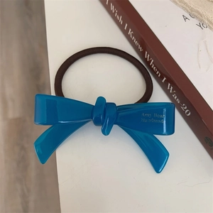 Gros plan d'un chouchou à nœud en acétate bleu avec lettrage fait main sur fond blanc