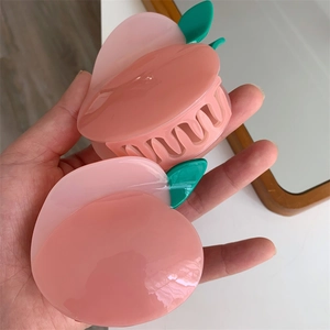Gros plan d'une pince à cheveux en acétate en forme de pêche rose avec détails de feuilles