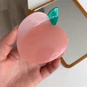 Gros plan d'une pince à cheveux en forme de pêche rose en résine avec des feuilles vertes