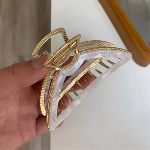 Close-up of golden metal hair claw clip with iridescent white acetate crescent inlay