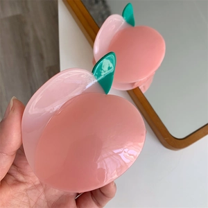 Pince à cheveux pêche rose translucide avec feuilles vertes vue dans un miroir