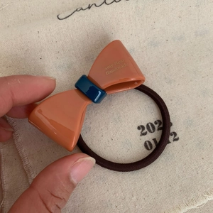 Detail of high-elasticity hair tie featuring orange acetate bow and logo engraving