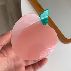Gros plan sur la pince à cheveux en acétate en forme de pêche avec dégradé de rose et feuille