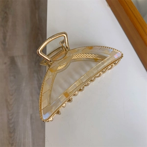 Detail of a large gold metal hair claw clip featuring marble texture acetate plates