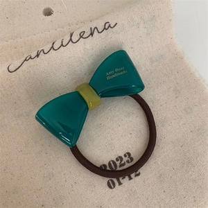 Detail of dark green acetate bow hair tie with handmade lettering on cream linen bag