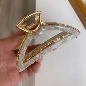 Detailed macro view of large gold metal hair claw clip with white marble acetate finish