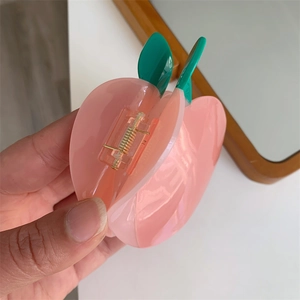 Détail du mini pince à cheveux en acétate en forme de pêche rose avec feuilles vertes