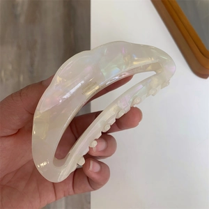 Detail of crescent acetate hair claw with iridescent pearl finish and handmade gold logo