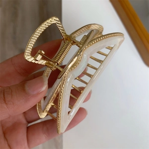 Detailed close-up of cream acetate bow hair claw clip with golden metal frame