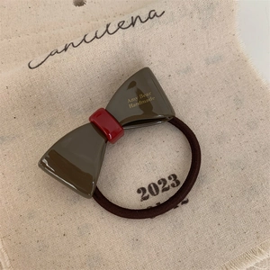 Detail of a brown resin bow hair tie with golden Amy Bear Handmade text on fabric background